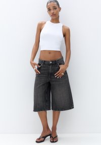 Čierne džínsy culottes s vysokým pásom a strapcami na leme, skombinované s priliehavým bielym crop topom a čiernymi plochými sandálmi. Hladká textura, ležérny dizajn.