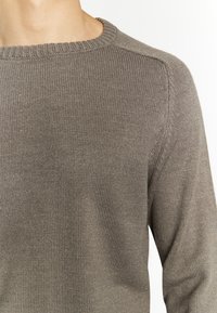 Maglione a coste marrone con scollo rotondo e texture sottile, caratterizzato da un design leggermente aderente e dettagli delle cuciture visibili.