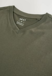 Olivgrön t-shirt med v-hals i vanlig passform, med en mjuk bomullstextur och en etikett som inkluderar varumärke och skötselinformation sydd innanför.