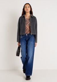 Γκρι cropped μπουφάν με φερμουάρ μπροστά, πουκάμισο από πλέγμα με καρό σχέδιο, μπλε τζιν παντελόνι φαρδιάς γραμμής και μαύρη τσάντα με λευκές πουά. Μαύρα παπούτσια.