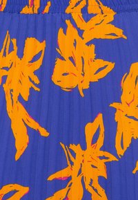 Formes florales abstraites orange vif sur un tissu bleu profond plissé avec une taille élastique froncée.