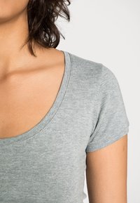 Šedé tričko s krátkým rukávem a širokým výstřihem, vyrobené z měkkého, mírně texturovaného materiálu, s přiléhavým střihem.