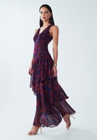 Flowy layered dress in sheer burgundy fabric with a floral pattern. Features a deep V-neck and asymmetrical hemline, paired with strappy heels.
