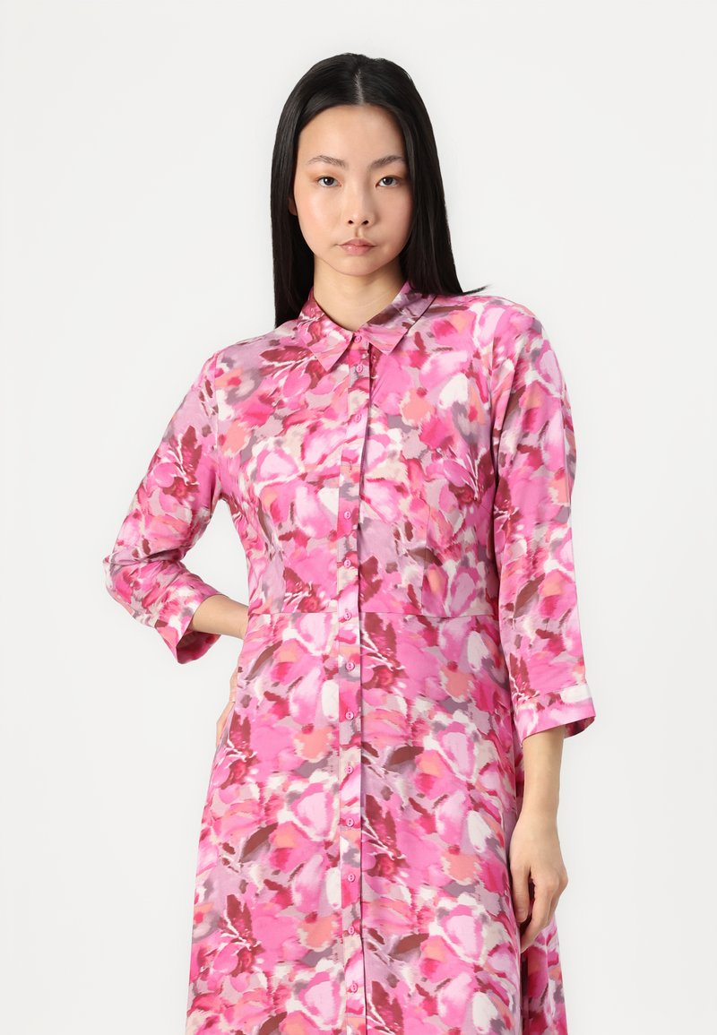 Różowa sukienka w kwiaty, wykonana z lekkiego materiału, z zapięciem na guziki z przodu, spiczastym kołnierzykiem i rękawami trzyczwartkowymi o płynnej formie.