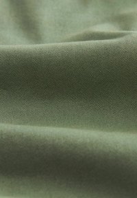 Tissu vert olive avec une surface lisse et texturée, présentant un motif de tissage diagonal. Le matériau semble durable et légèrement réfléchissant.