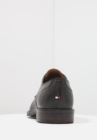 Chaussure habillée en cuir noir avec un bout rond, un petit talon, et un intérieur beige. Dispose d'un petit patch de logo coloré à l'arrière.