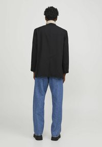 Zwarte blazer met een enkele achterkant vent, gecombineerd met losse blauwe denim jeans. De stof heeft een gladde textuur.