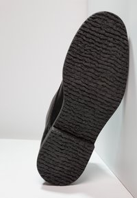 Czarna guma podeszwy butów z teksturowanym, rowkowanym wzorem dla lepszej przyczepności, z lekko podniesioną tęgością i zaokrąglonym obcasem.