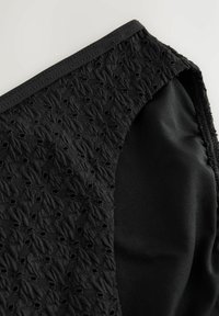 Crni materijal s teksturiranom, uzorkovanom mrežicom s jedne strane i glatkim materijalom s druge, sašiven s elastičnom trakom duž ruba.