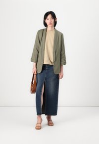 Olivengrøn, let blazer over en beige skjorte, parret med en denim maxi-nederdel med en frontslids. Brun crossbody taske og lysebrune sandaler.