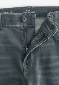 Szare dżinsy z zamkiem błyskawicznym i zapięciem na guzik. Cechy to kontrastowe szwy oraz miękka, teksturowana powierzchnia.