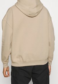 Sudadera beige de gran tamaño en tela suave con capucha ajustable con cordón, puños y dobladillo acanalados, con un corte holgado para mayor comodidad.