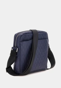 Sac bandoulière bleu marine avec un motif texturé géométrique, doté d'une fermeture éclair et d'une bandoulière ajustable. Design en forme de carré.