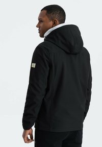 Veste noir zippée avec capuche, doublure blanche et poignets élastiques. Présente un petit patch logo sur la manche gauche. Texture lisse et design ajusté.