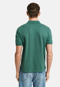Zielona koszulka polo z krótkim rękawem, wykonana z bawełny, z prążkowanym kołnierzykiem i gładką teksturą. Noszona z jasnoniebieskimi dżinsami.