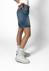 Denim miniskjørt i lyseblått, knelangt, med tilpasset midje, to baklommer og broderte sømmer. Kombinert med hvite joggesko og sokker.