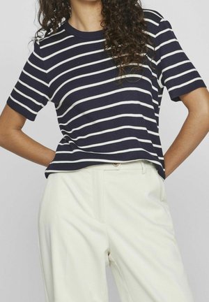 Navy and white striped short-sleeve top with a round neckline, textured ribbed fabric, paired with cream-colored high-waisted trousers.
