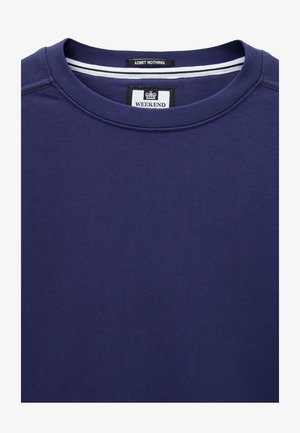 Granatowa bluza z okrągłym dekoltem, z czarnymi i białymi metkami wewnątrz kołnierza z napisem "ADMIT NOTHING" i "WEEKEND" oraz ikoną korony.