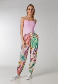 Lichtroze geribde tanktop gecombineerd met multicolor bloemenpatroon joggingsbroek met een elastische tailleband en trekkoord, gedragen met witte sneakers.
