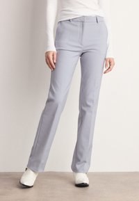 Jasnoszare dopasowane spodnie o gładkiej fakturze, prostym kroju nogawki i subtelnymi bocznymi kieszeniami, w zestawieniu z białym obuwiem.