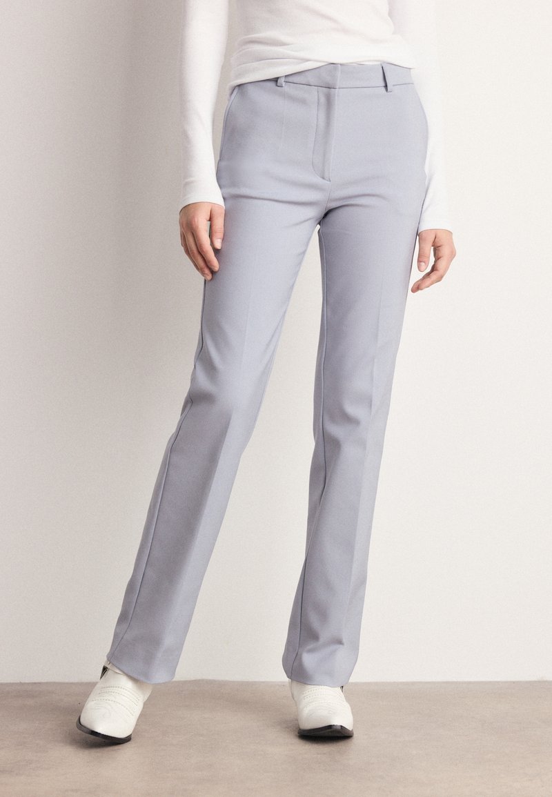 Jasnoszare dopasowane spodnie o gładkiej fakturze, prostym kroju nogawki i subtelnymi bocznymi kieszeniami, w zestawieniu z białym obuwiem.