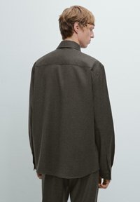 Mørkebrun skjorte med knapper lavet af struktureret stof, med en klassisk krave og lange ærmer med lukkede manchetter, set fra ryggen.
