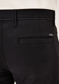 Black pants with a smooth texture, featuring a back pocket, belt loops, and a small tag near the waistband. Clean stitching details.