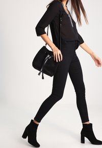 Blusa nera a maniche lunghe con scollatura a V, abbinata a jeans neri aderenti e stivaletti. Una borsa in suede nero con dettaglio a frange.