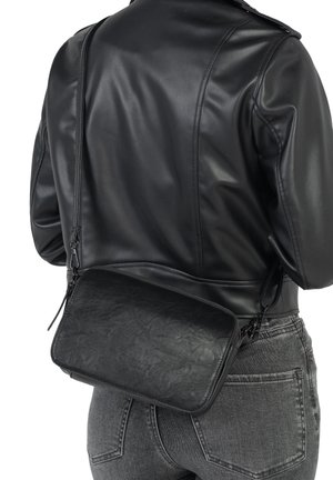 Sac à bandoulière synthétique noir avec une surface texturée, fermeture à glissière et sangle réglable, porté sur une veste en cuir noir.