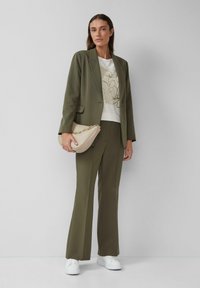 Blazer et pantalon ajustés couleur vert olive, associés à un haut graphique blanc et un sac à main beige. Des baskets blanches complètent le look.