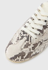 Αθλητικό παπούτσι με μοτίβο δέρματος φιδιού, σόλα από καουτσούκ σε κρεμ απόχρωση και κορδόνια από λευκό βαμβάκι, με υφή που θυμίζει λέπια σε αποχρ ώσεις του γκρι και μπεζ.