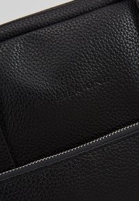 Schwarze, strukturierte Ledertasche mit Reißverschluss, versehen mit geprägtem Text "PIER ONE" und einem glatten Innenfutter. Kompaktes und elegantes Design.