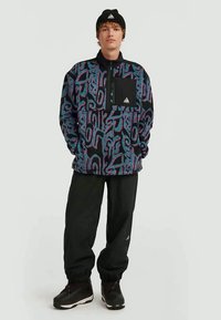 Fleece pullover with a black and blue abstract pattern, half-zip closure, chest pocket, paired with loose black pants and black boots.