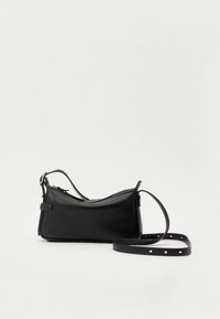 Svart läderaxelväska med justerbar rem och dragkedjesstängning mot en enfärgad vit bakgrund.