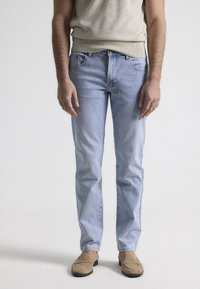 Jeans de denim azul claro con corte recto, bolsillos frontales y un ligero desgaste. Combinados con mocasines color marrón claro y una camiseta sin mangas beige.