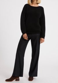 Czarny sweter o prążkowanej strukturze z szerokim dekoltem i długimi rękawami, w połączeniu z czarnymi spodniami o szerokich nogawkach i brązowymi botkami na obcasie.