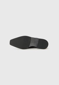 Semelle noire d'une chaussure, présentant une forme plate avec une texture lisse. La construction est robuste, avec un minimum de détails et un design épuré.