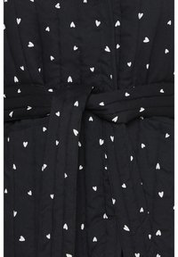 Robe en tissu noir matelassé avec un motif de cœurs blancs ; comprend une ceinture en tissu assortie et des détails de couture verticale pour la texture.