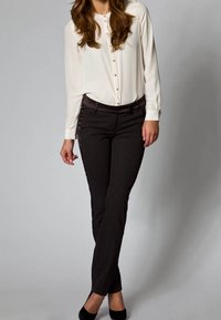 White button-up blouse with long sleeves and gold buttons, paired with black fitted trousers and black heels, against a neutral background.