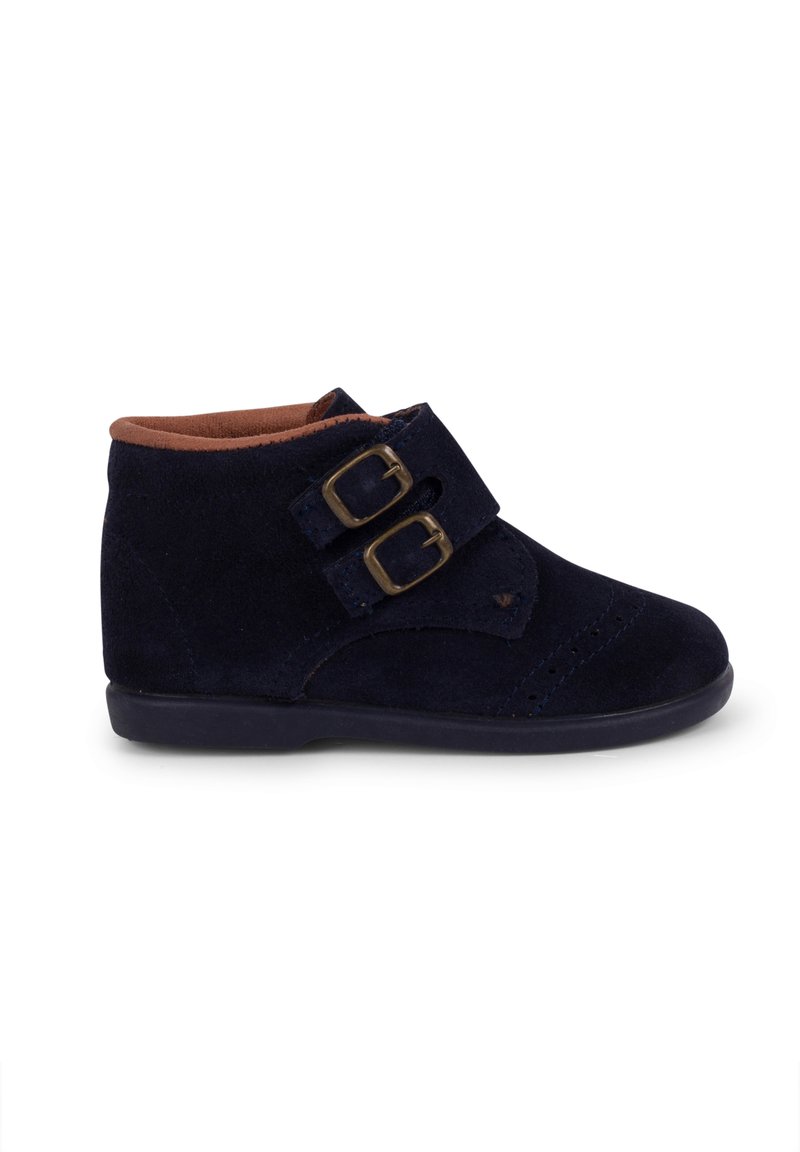 Bocanci de gleznă din suede bleu marin, cu curele duble cu catarame, vârful rotund și un căptușel interior maro în contrast. Talpă plată din cauciuc cu un profil subtil.