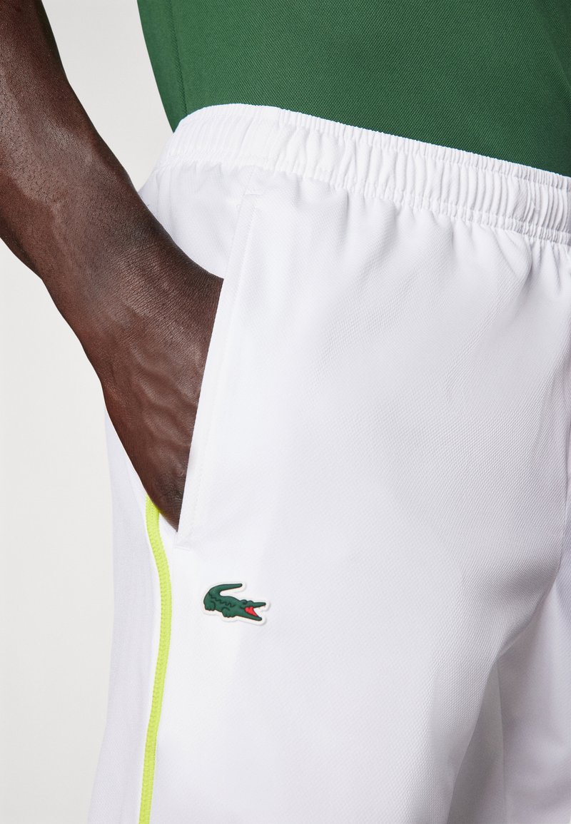 Białe szorty z elastycznym pasem i zielonymi akcentami po bokach. Posiadają zielone logo krokodyla na lewej nodze oraz kieszeń.