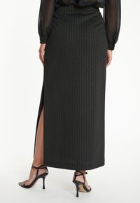 Zwarte maxi-jurk met verticale zilveren streepjes, voorzien van een split aan de zijkant en een aangesloten taille. Het materiaal lijkt glad met een lichte glans.
