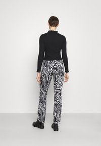 Svart rutig långärmad topp med volangkrage, kombinerad med högmidjade byxor med ett djärvt svart och vitt virvlande mönster. Svarta skor.