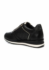 Zapatilla negra con diseño floral perforado, detalles en dorado y un talón texturizado. Presenta una suela blanca y negra, cordones en la parte delantera y un cuello acolchado.