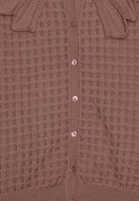 Cardigan marron avec une texture tricotée et un motif floral. Il dispose d'une fermeture à boutons et de boutons ronds légers. Agrémenté d'un nœud.