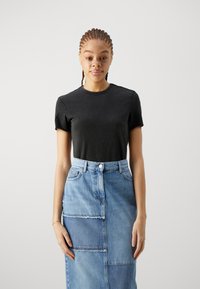 T-shirt nera a maniche corte abbinata a una gonna di jeans a vita alta, lunghezza al ginocchio, con un motivo patchwork in tonalità di blu chiaro e scuro.