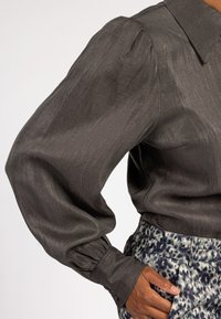 Donkergrijze blouse met een gestructureerd oppervlak, met een klassieke kraag en opbollende mouwen, gecombineerd met geblokte broeken.