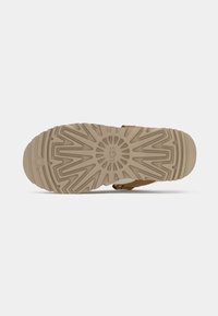 Brune sandal med en flad, struktureret gummisål med et solstrålemønster. Justerbar rem med en metalspænde for pasform.