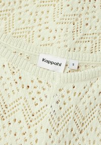 Krämfärgad stickad tröja med ett geometriskt öppet mönster, ribbad halsringning och en Kappahl-etikett som anger storlek 'S'.