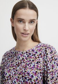 Floral blouse with a round neckline; features purple, black, and brown flowers on a light blue background; lightweight fabric with subtle texture.